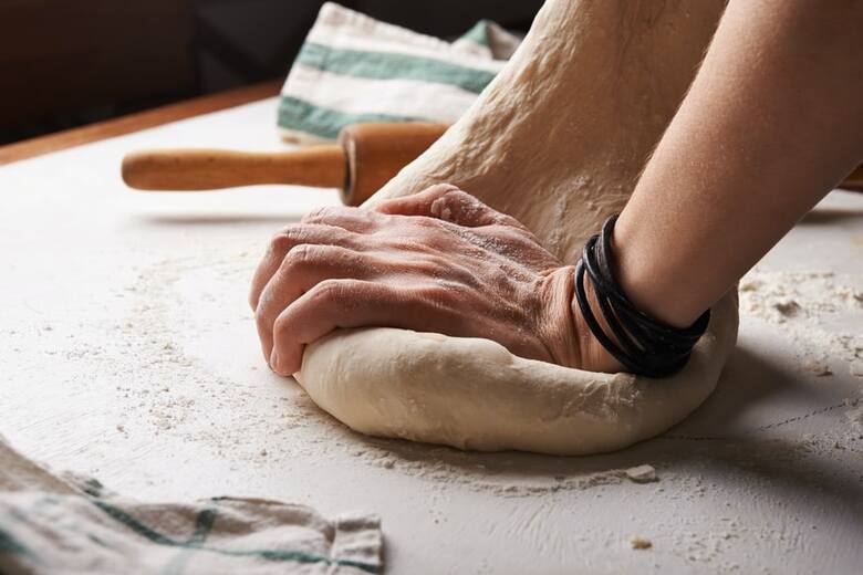 Podrośnięte ciasto przełóż na stolnicę wysypaną mąką, wyrabiaj jeszcze ok. 2 min i uformuj ręcznie kształt pizzy.