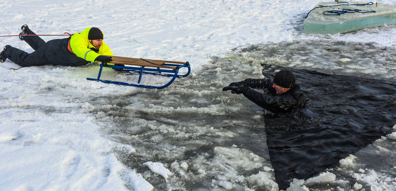 Ratownik podaje tonącemu wiosło (może być też kij, gałąź, koc) i pomaga mu wypełznąć na lód.