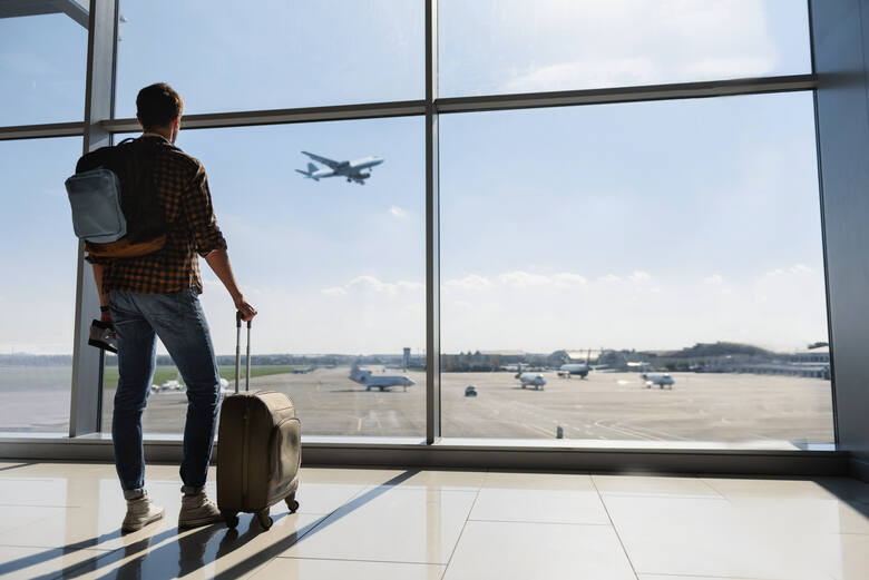 Mężczyzna stoi przy oknie na lotnisku i obserwuje samolot