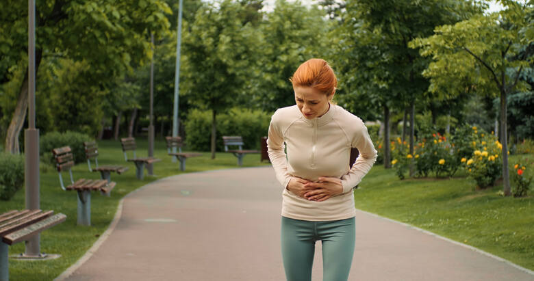 Młoda kobieta cierpi na ból brzucha podczas biegania w parku
