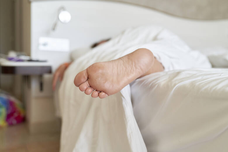 Osoba leżąca na białym łóżku pod białym kocem z wystającą jedną nogą