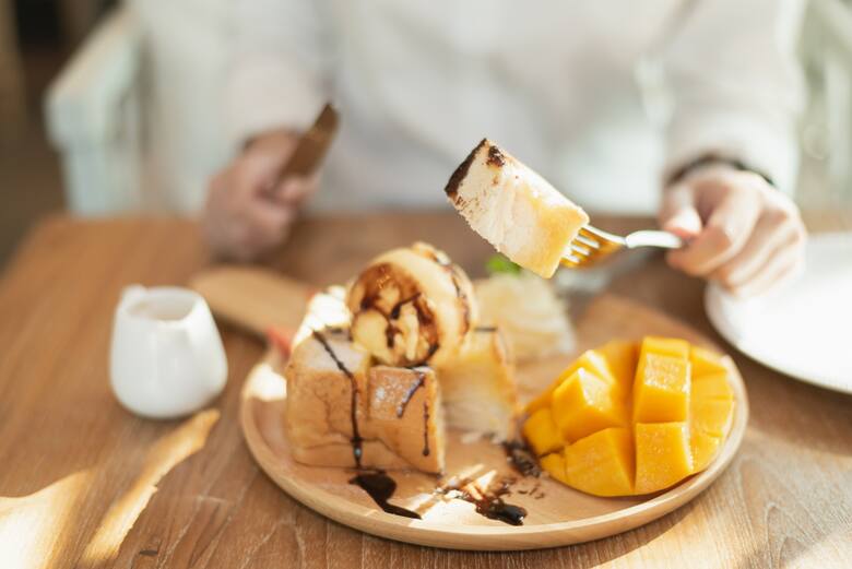 Zbliżenie na talerz ze słodką przekąską i mango i ręce kobiety przy stole