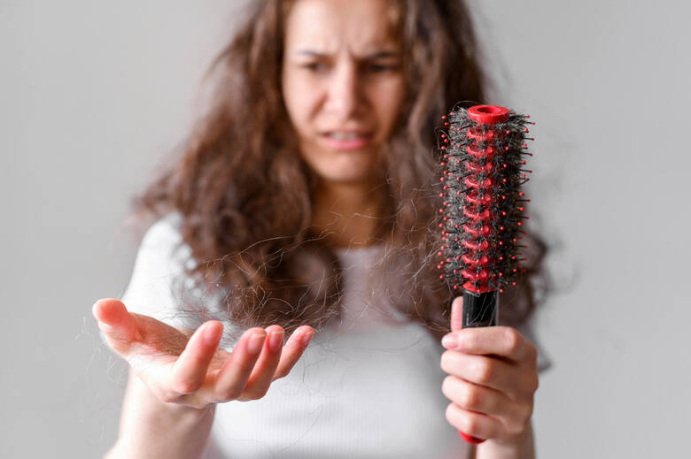 Młoda kobieta z przerażoną miną patrzy na kępkę włosów po czesaniu szczotką