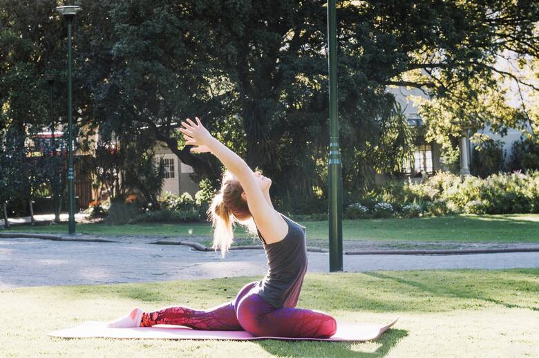Młoda kobieta robi ćwiczenie rozciągające plecy i nogi na macie w parku