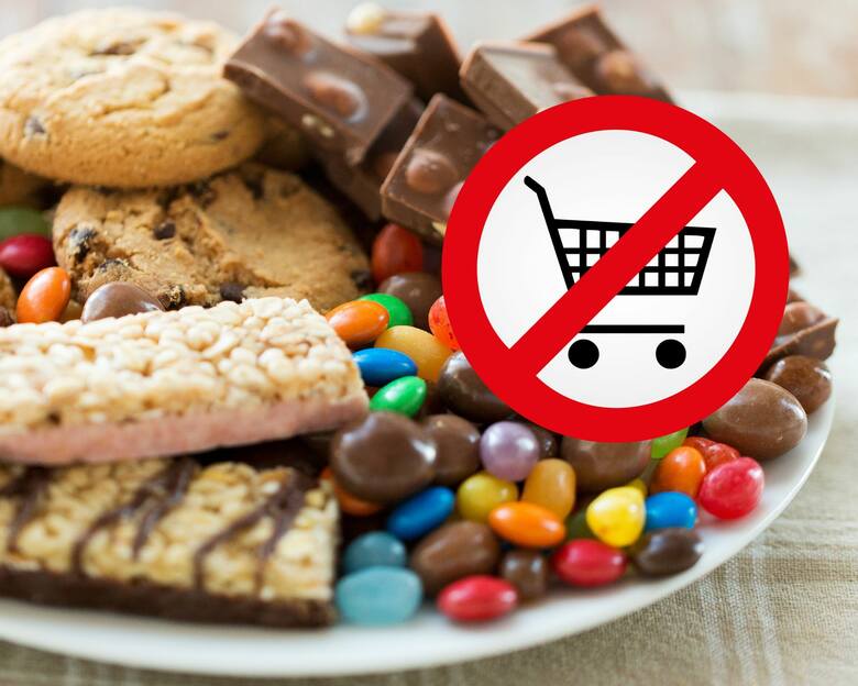 Różne rodzaje przemysłowych słodyczy na talerzu i znak zakazu kupowania