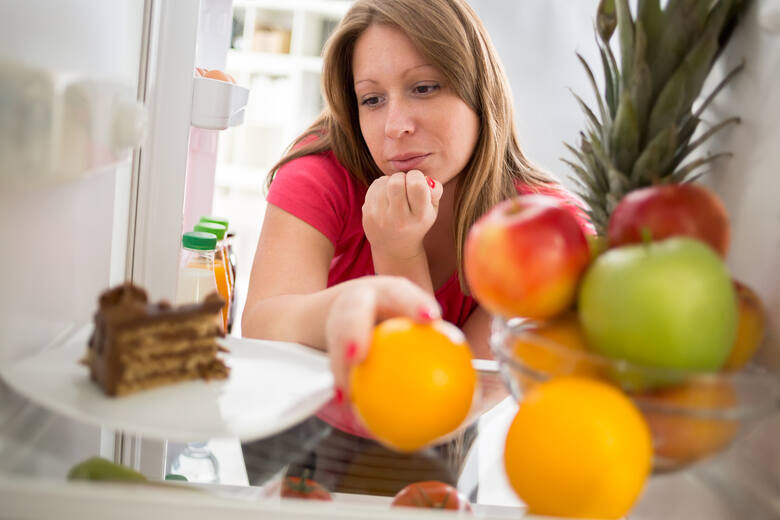 Młoda kobieta patrzy w lodówce na ciasto i owoce