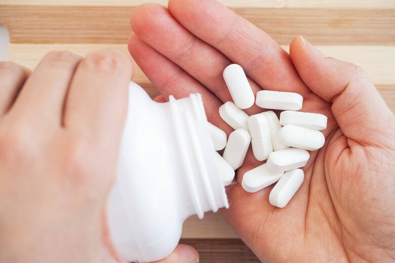 Białe tabletki w opakowaniu i na dłoni