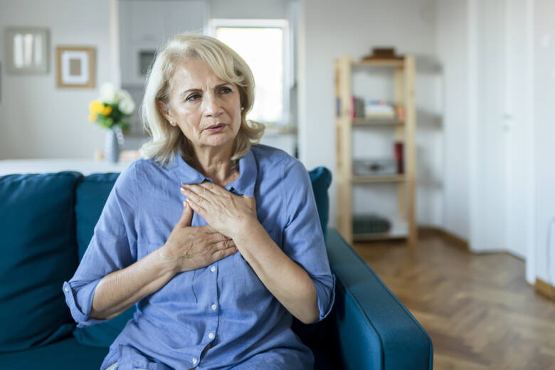 Starsza kobieta z bólem klatki piersiowej trzyma dłonie na wysokości mostka