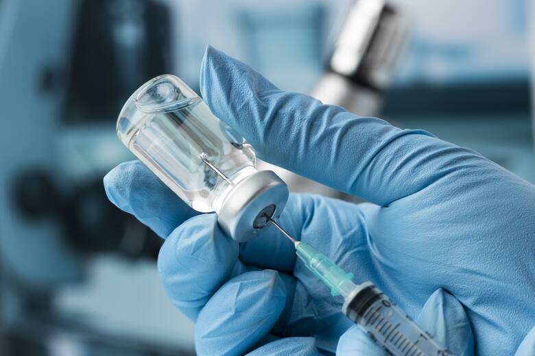 Lekarz w rękawiczce nabiera strzykawką szczepionkę z buteleczki