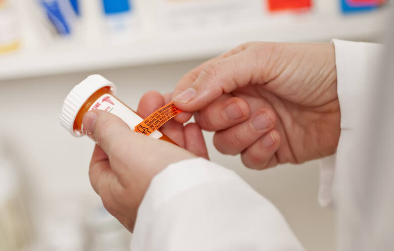 Farmaceuta nakleja etykietę z ostrzeżeniem na opakowaniu leku