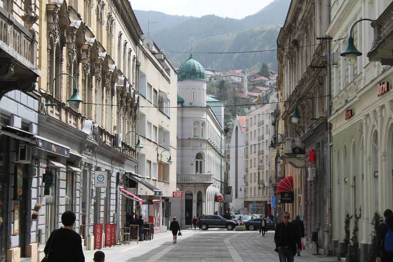 Sarajewo, widok sprzed katedry katolickiej. Wokół kamienice, pamiętające czasy cesarza Franciszka Józefa, w tle minaret meczetu. Dachy i góry.
