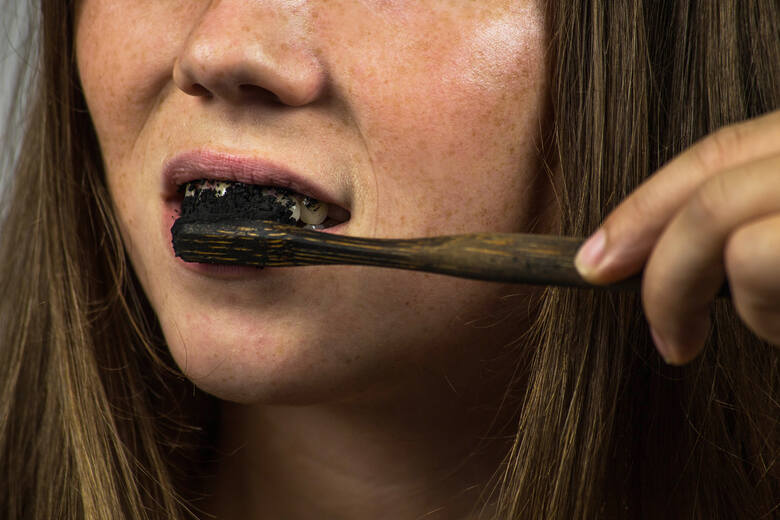 Młoda kobieta myje zęby czarną pastą węglową