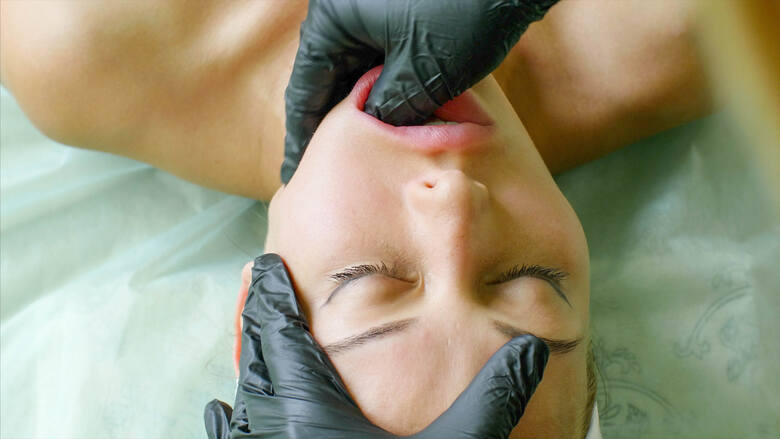  Młoda kobieta na leżance podczas masażu transbukalnego wykonywanego w jednorazowych rękawiczkach