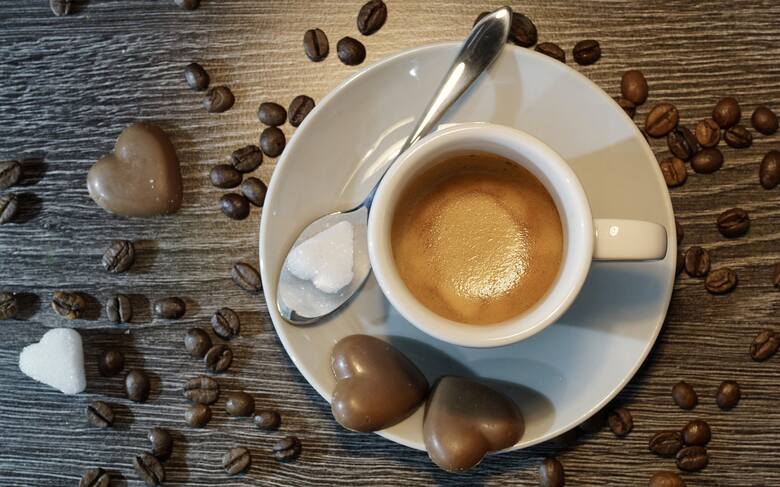 Filiżanka kawy z cukrem na łyżeczce i ciasteczkami w kształcie serca na spodku