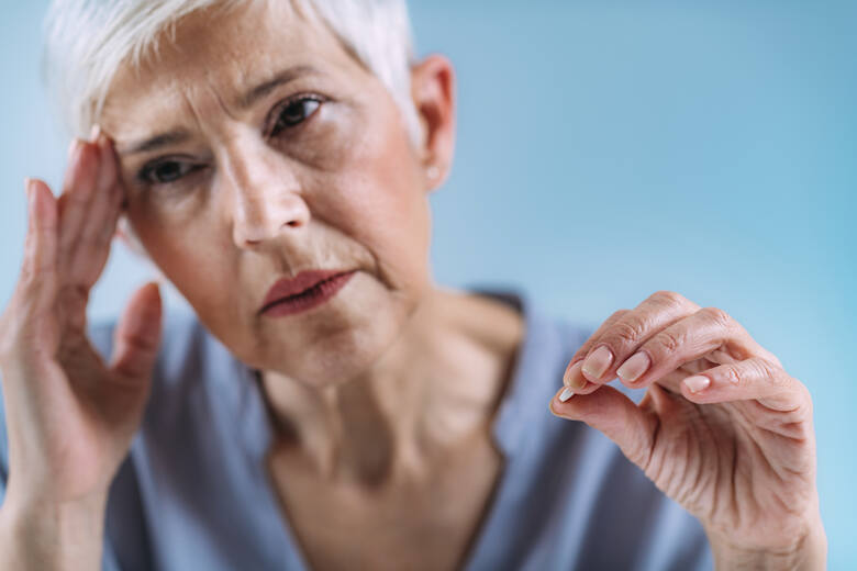 Kobieta w średnim wieku z bólem głowy i tabletką w ręku