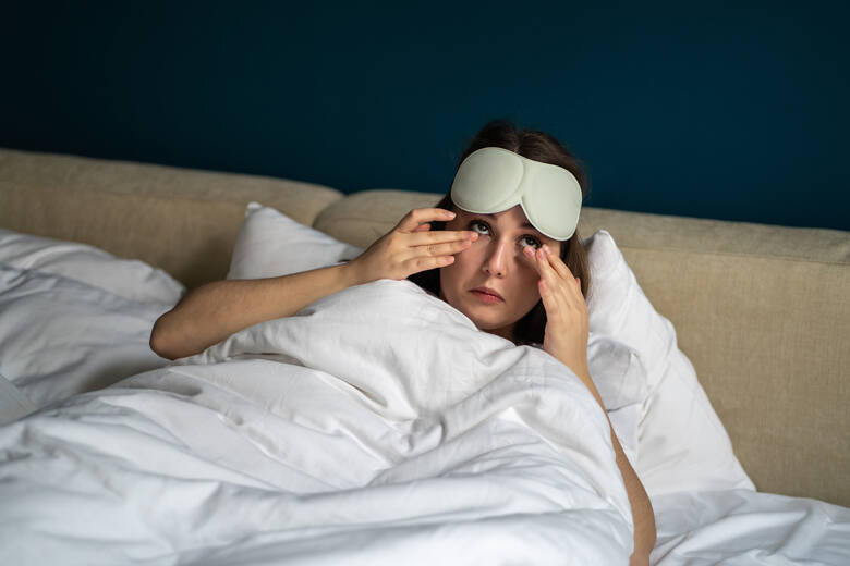 Śpiąca kobieta budząca się w łóżku, zdejmująca maskę na oczy po nocy