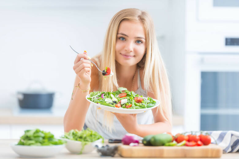 Młoda kobieta je sałatkę przy stole pełnym świeżych warzyw