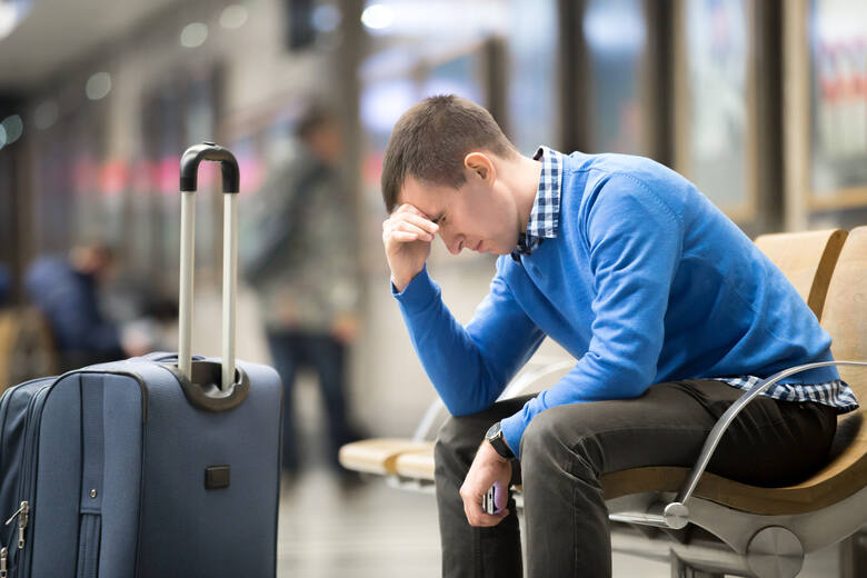 Młody mężczyzna siedzi zmęczony z walizką na lotnisku
