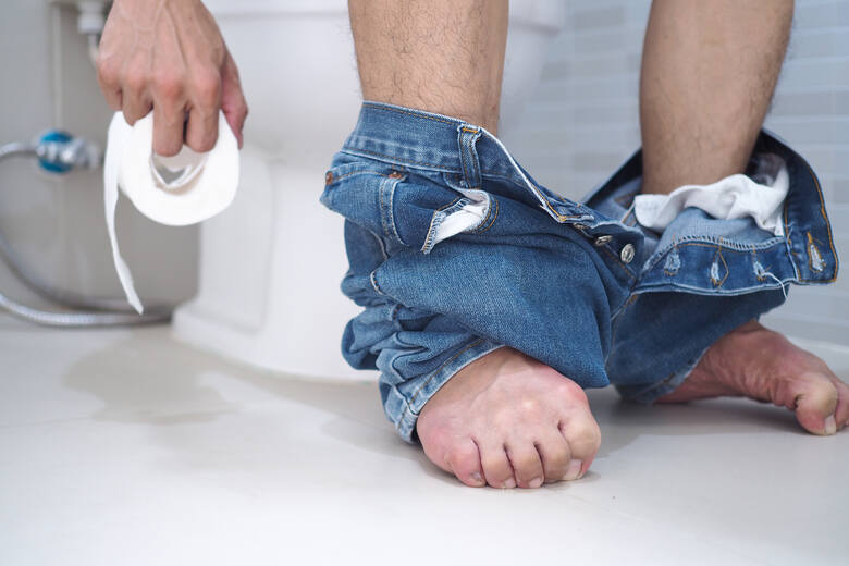 Zbliżenie na męskie stopy i papier toaletowy w toalecie