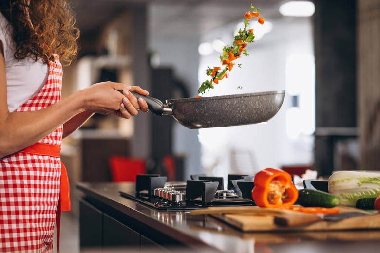 Kobieta smaży warzywa na kuchence gazowej