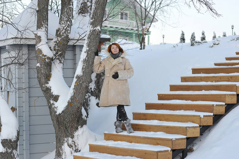Kobieta w kożuchu stoi na zaśnieżonych schodach