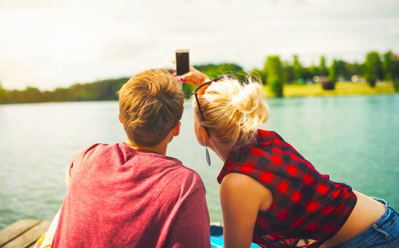 Para robiąca zdjęcie smartfonem nad jeziorem