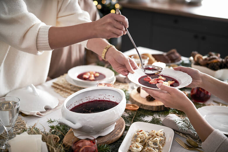 Bożonarodzeniowy stół z jedzeniem, kobieta nalewa barszcz czerwony do talerza