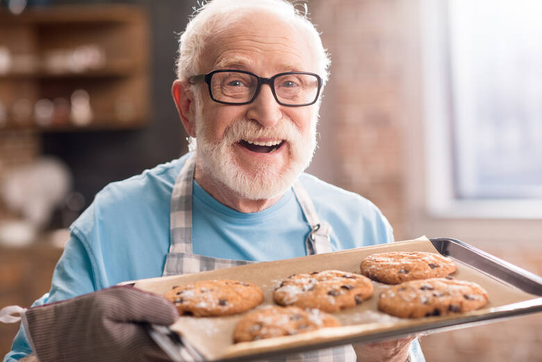 Starszy uśmiechnięty mężczyzna z blaszką upieczonych ciastek