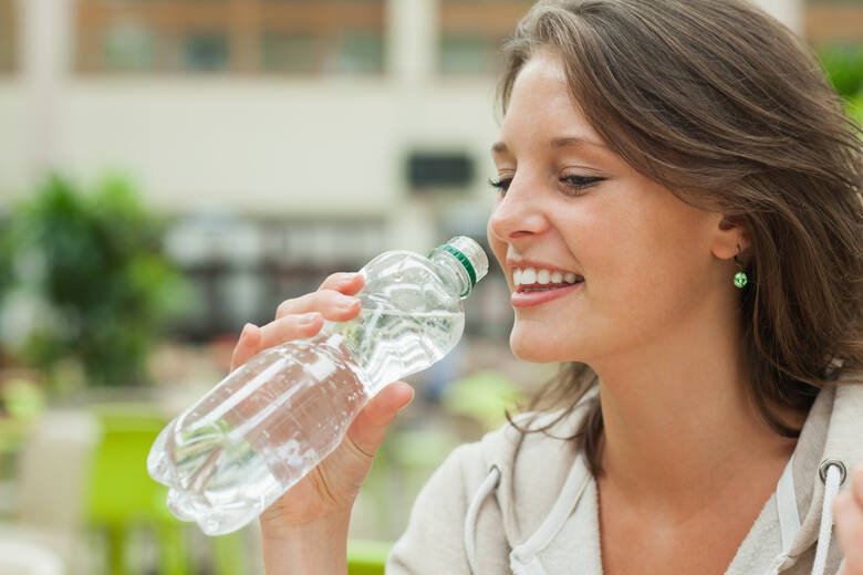 Młoda kobieta pije wodę prosto z plastikowej butelki