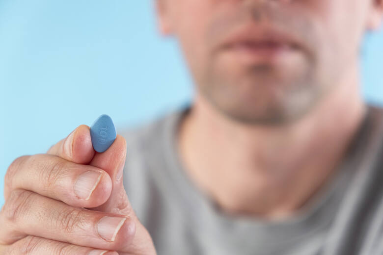Mężczyzna trzyma niebieską tabletkę w palcach dłoni
