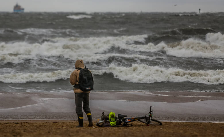 Turysta z rowerem patrzy na wzburzone morze