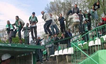Kibice Radomiaka próbują przeskakiwać przez wysokie ogrodzenie na stadionie.