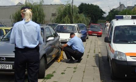 Strażnicy zakładają blokady na koła nieprawidłowo zaparkowanych samochodów.