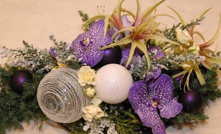 Płaski stroik na stół świąteczny stół, bazą są gałązki ogrodowych iglaków, a ozdobą kwiaty Orchidea Vanda i amarylis, do tego ręcznie malowana bombka