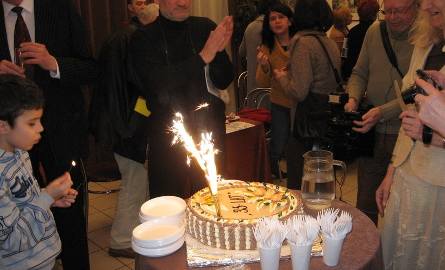 Płoną świeczki na jubileuszowym torcie, zapala je wnuk malarki Tomek.