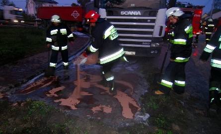 Strażacy posypują jezdnię specjalnym proszkiem, wchłaniającym rozlany olej napędowy.