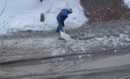 Odśnieżając chodnik ta kobieta zgarnia śnieg na ulicę