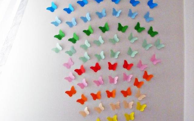 Kolorowe motyle wnoszą powiew wiosny do wnętrza. Dekoracja jest wycięta z kolorowego papieru i przyklejona do ściany taśmą dwustronną.