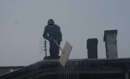 Pracownik odśnieża dach bez żadnego zabezpieczenia.